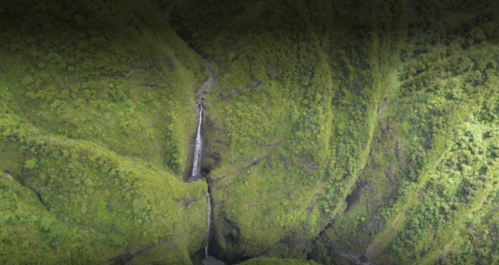 Aerial view of a lush green landscape with a small waterfall cascading down a steep hillside.