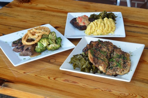 Three plates of food: grilled meat, broccoli, onion rings, collard greens, and creamy side dishes on a wooden table.