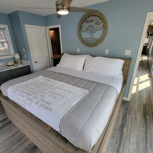 A cozy bedroom with a large bed, light blue walls, and a decorative wall art piece. Natural light fills the space.