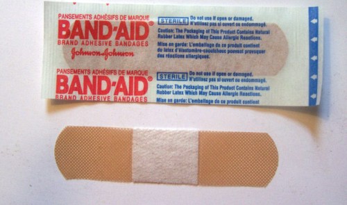 A Band-Aid package with a single adhesive bandage displayed beside it, featuring a beige color and a sterile label.