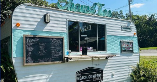 A vintage-style food truck with a teal and white exterior, featuring an open window and a chalkboard menu.