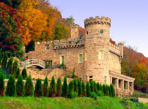 A stone castle with a turret, surrounded by colorful autumn trees and neatly trimmed hedges.