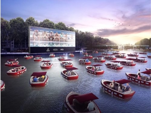 A scenic view of boats on a river, with a large screen displaying a film in the background.