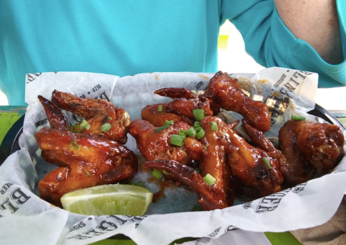 A plate of spicy chicken wings garnished with green onions and a lime wedge, served in a basket.