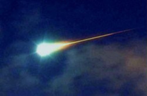 A bright meteor streaks across a dark sky, leaving a glowing trail behind it.