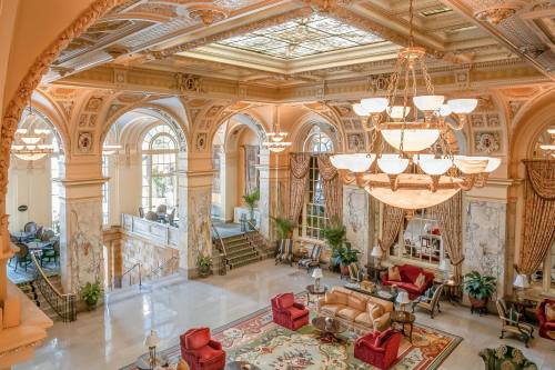 Elegant hotel lobby with ornate architecture, plush seating, and large windows, featuring a grand chandelier.