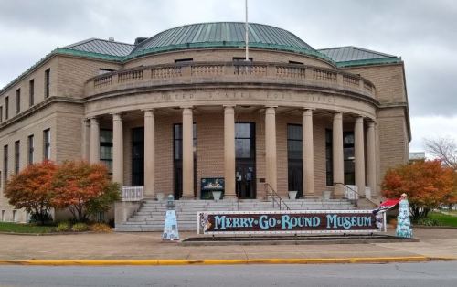 Historic building with columns, labeled as the Merry-Go-Round Museum, featuring colorful decorations outside.