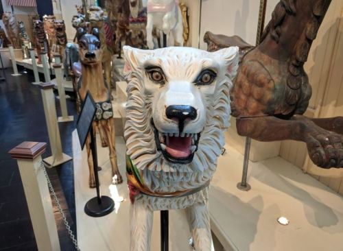 A close-up of a carved wooden dog figure with a fierce expression, surrounded by other decorative animal sculptures.