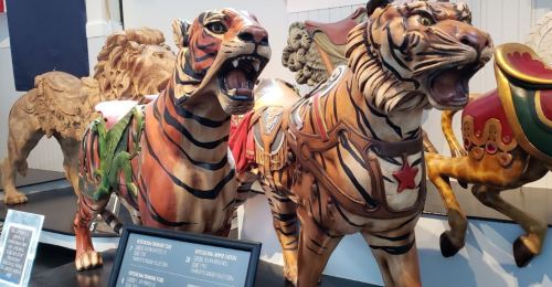 Two intricately carved wooden tigers with vibrant colors and detailed designs, displayed in a museum setting.