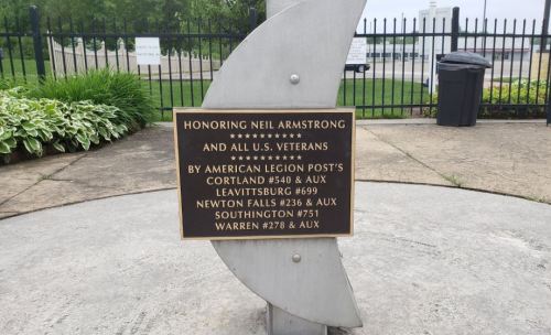 Plaque honoring Neil Armstrong and U.S. veterans, displayed on a monument with a curved metal design.