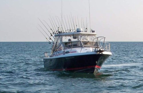A fishing boat with multiple rods is cruising on calm waters under a clear sky.