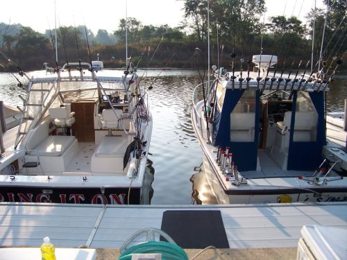 Two fishing boats docked side by side at a calm marina, surrounded by trees and reflecting water.