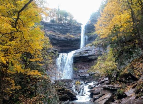 A scenic waterfall cascading down rocky cliffs, surrounded by vibrant autumn foliage.