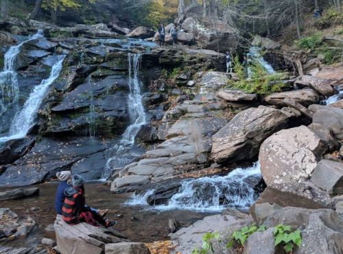 A serene waterfall cascades over rocky terrain, with people exploring the area and enjoying nature.