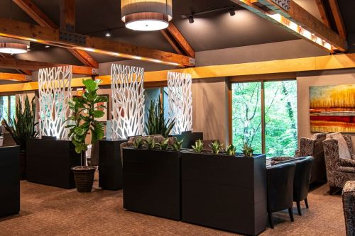Modern restaurant interior featuring decorative plant dividers, large windows, and cozy seating areas.