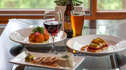 A table setting with two plates of gourmet food, a glass of red wine, and a beer, all in a cozy dining atmosphere.