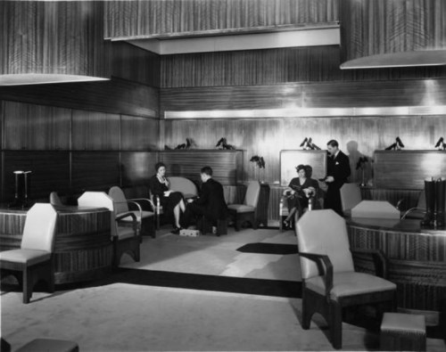A stylish vintage lounge with four people seated, elegant furniture, and high-heeled shoes displayed on a table.