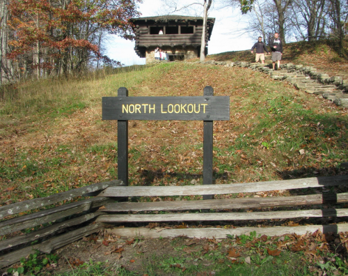 Sign for "North Lookout" in front of a wooden lookout tower, surrounded by trees and a grassy hill.