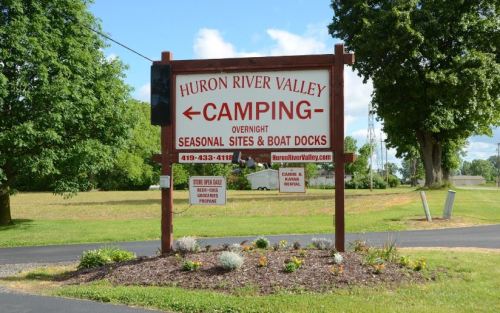 Sign for Huron River Valley Camping, featuring directions and contact information, surrounded by greenery.
