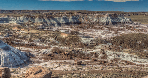 A vast, colorful landscape of layered hills and rocky formations under a clear blue sky.