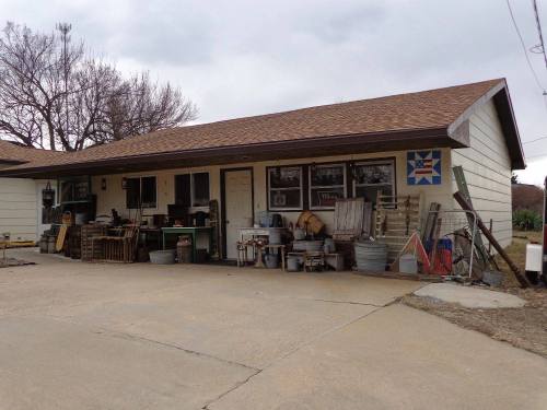 A rustic building with a brown roof, featuring various tools and containers outside, set against a cloudy sky.