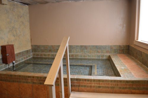 A small indoor spa area featuring a tiled hot tub and a bench, with a window letting in natural light.