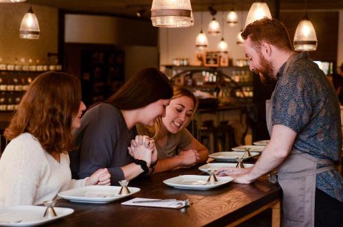 A group of three women at a restaurant table engage with a male server, discussing their meal options.