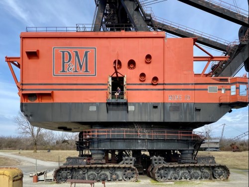 A large orange and black industrial crane with tracks, featuring the letters "P&M" on its side, set against a blue sky.