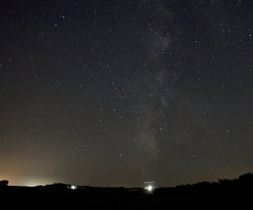 A starry night sky with the Milky Way visible, and distant lights from a landscape below.