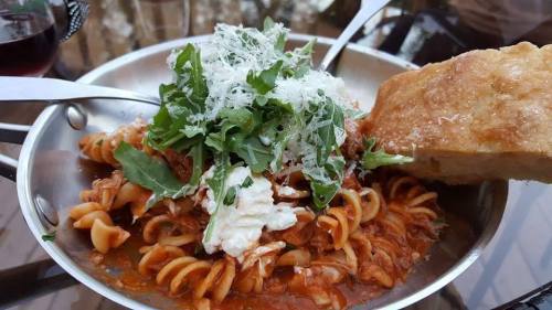 A plate of pasta with meat sauce, topped with arugula and cheese, alongside a piece of bread.