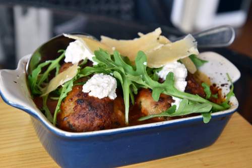 A dish of meatballs topped with arugula, dollops of ricotta, and shaved Parmesan in a blue baking dish.