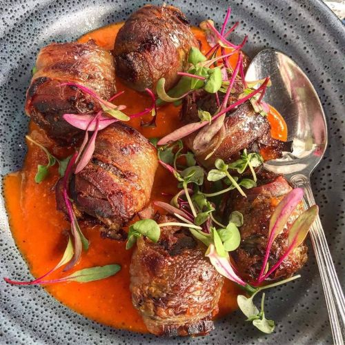 A plate of savory meat rolls garnished with microgreens, served in a rich red sauce.