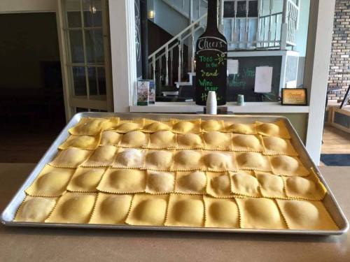 A large tray filled with neatly arranged uncooked ravioli, ready for cooking.