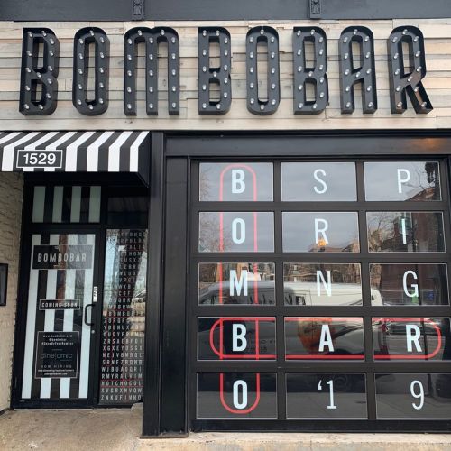 Exterior of Bombobar, featuring a large sign with the name in bright lights and a striped awning.
