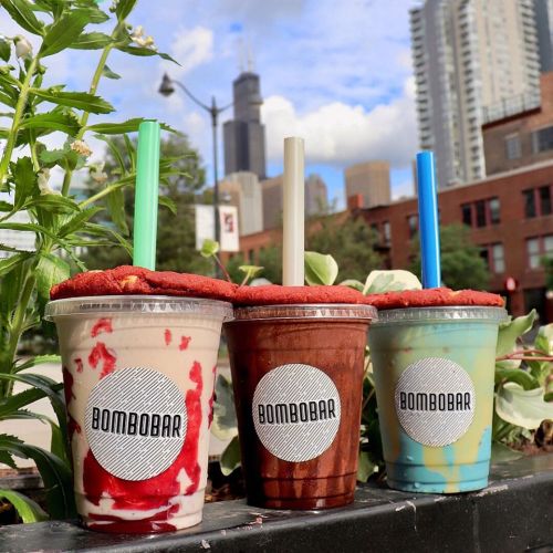 Three colorful drinks with whipped cream and cookie rims sit on a ledge, with a city skyline in the background.