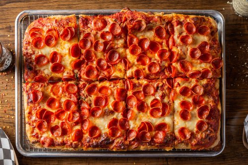 A rectangular pizza topped with pepperoni slices, baked to a golden brown, on a wooden table.