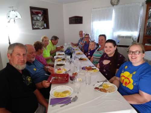 A group of people enjoying a meal together at a long table, with plates of food and drinks in a cozy dining room.
