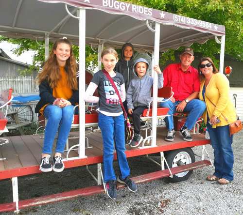 A group of five people, including children and adults, sitting on a buggy ride in a park setting.