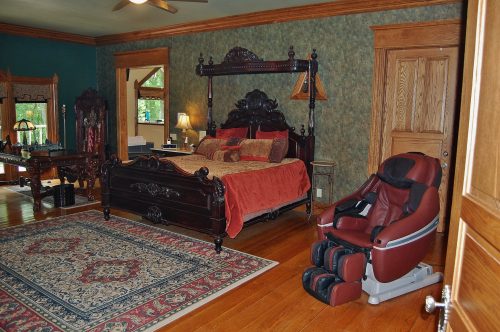 A luxurious bedroom featuring a four-poster bed, ornate decor, a massage chair, and a patterned area rug.