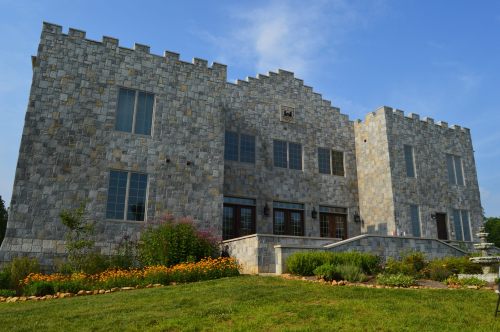 A large stone castle-like building with a landscaped garden and blue sky in the background.