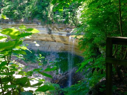 A serene waterfall cascading down rocky cliffs, surrounded by lush green foliage and trees.