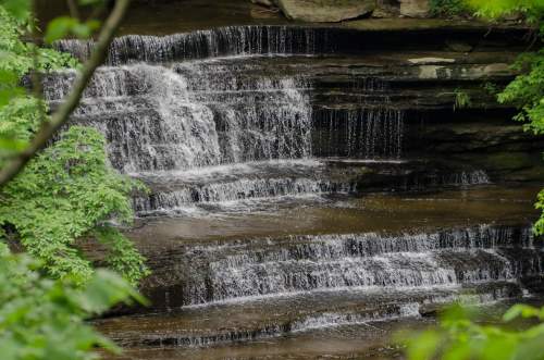 A serene waterfall cascading over rocky steps, surrounded by lush green foliage.