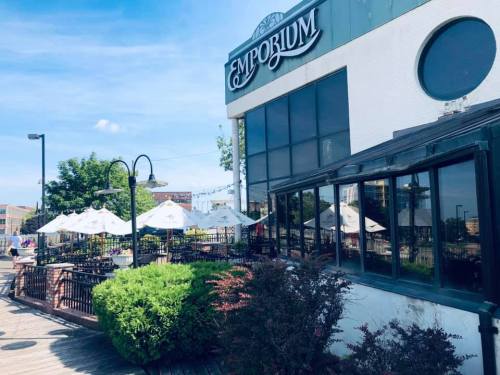 Exterior view of Emporium restaurant with outdoor seating, umbrellas, and greenery under a clear blue sky.
