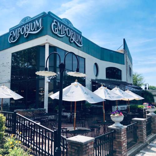 Exterior of a restaurant named "Emporium," featuring outdoor seating with umbrellas and a sunny blue sky.