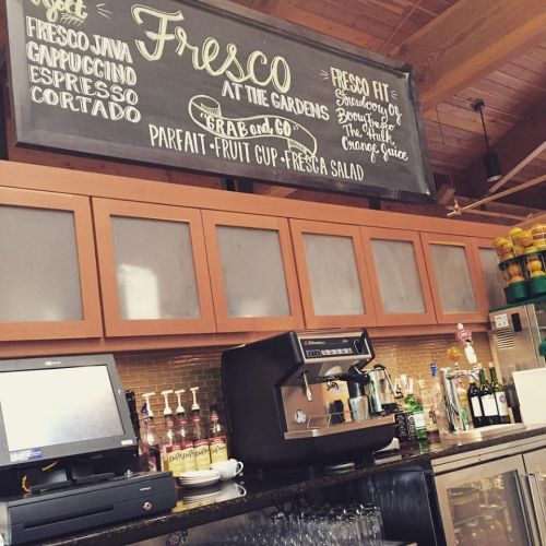 A café counter with a menu board displaying items like espresso, parfaits, and fresh juices.