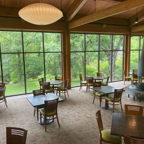 A spacious dining area with wooden tables and chairs, large windows showcasing a green outdoor view.