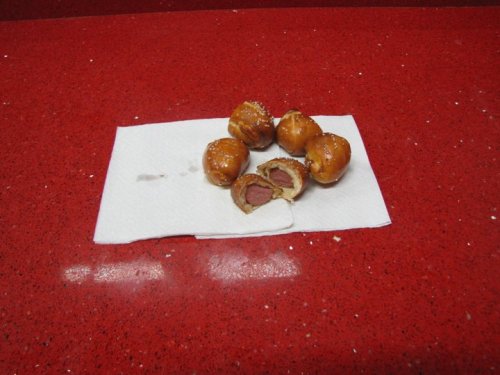 Five golden-brown, bite-sized snacks on a paper towel, with one cut open to reveal a sausage filling.