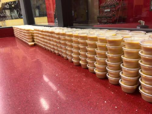 A long row of small cups filled with a creamy sauce, lined up on a red countertop.