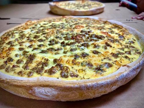 Two freshly baked pizzas with a golden crust and a cheesy, herb-topped surface, resting on a cardboard box.