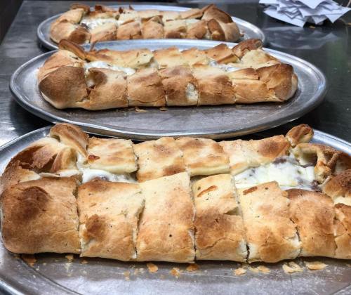 Three trays of freshly baked, golden-brown stuffed bread, cut into squares, resting on metal plates.